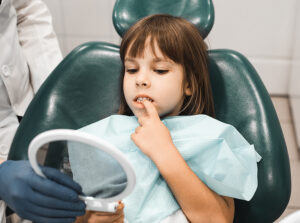 Young girl sitting in dental chair using a hand mirror to look at her teeth