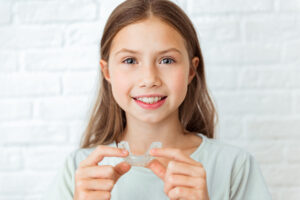 Smiling young girl holding orthodontic appliance